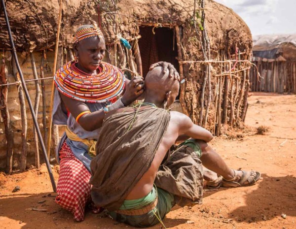 Masai woman piercing ear of safari guide in village